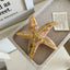 Tan marbled starfish hair clip with yellow dots and "sea star" text, resting in a gray tray