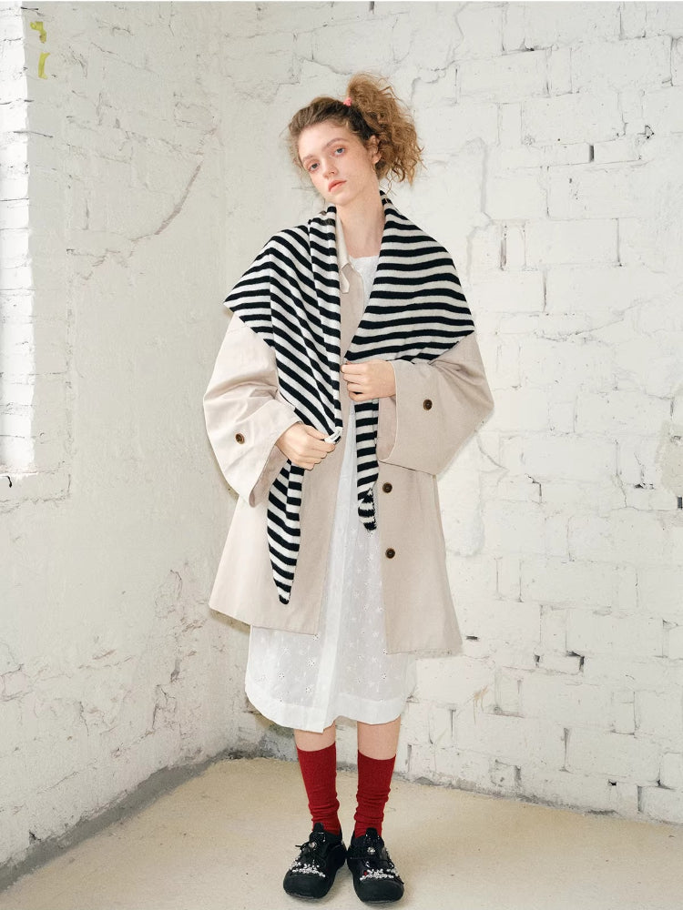 Full body shot of a model wearing a beige coat and black and white striped scarf