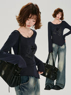Full body shot of a woman in a dark blue long-sleeve top and distressed jeans, holding a black handbag.