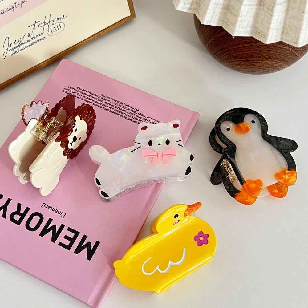 collection of animal hair claw clips including a cat, lion, penguin, and duck arranged on a pink book