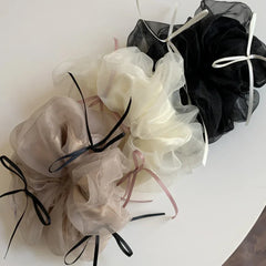 Overhead view of three large scrunchies in ivory, taupe, and black, showcasing their textures and ribbon details.