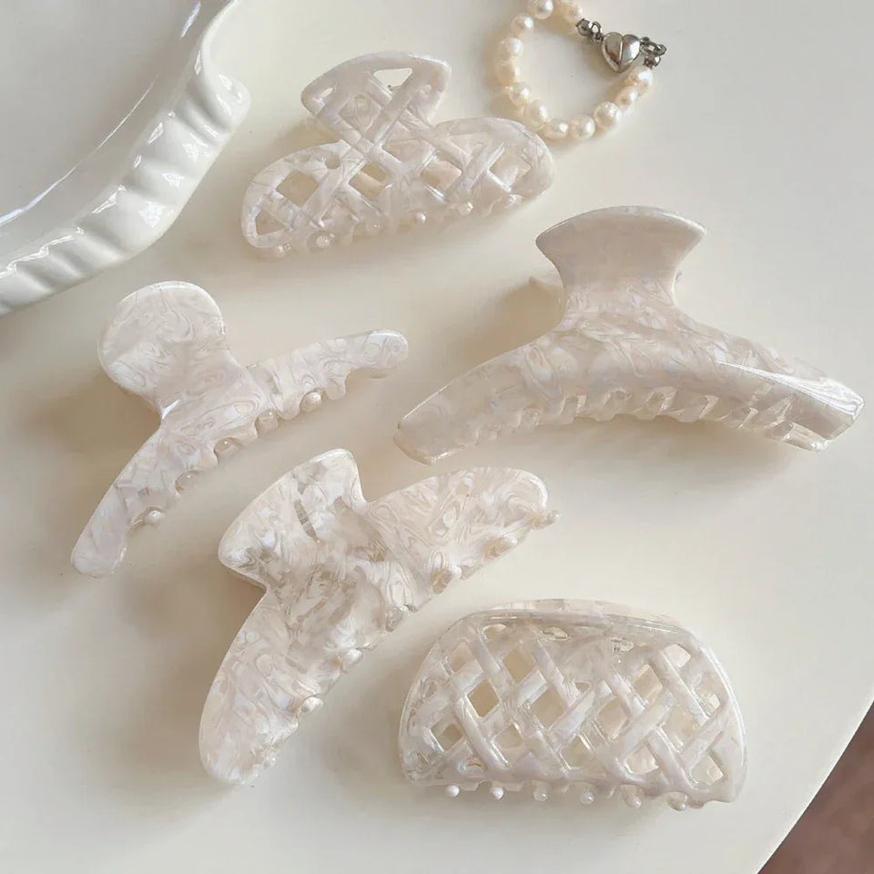 A collection of cream-colored marbled acetate hair clips and a pearl bracelet arranged on a light surface. Secondary image