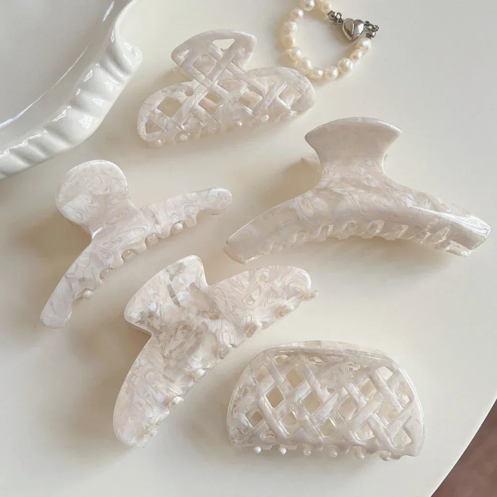 A collection of cream-colored marbled acetate hair clips and a pearl bracelet arranged on a light surface.