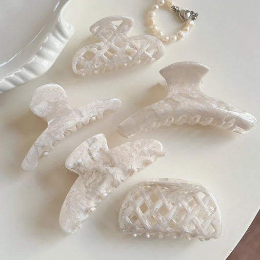 A collection of cream-colored marbled acetate hair clips and a pearl bracelet arranged on a light surface.