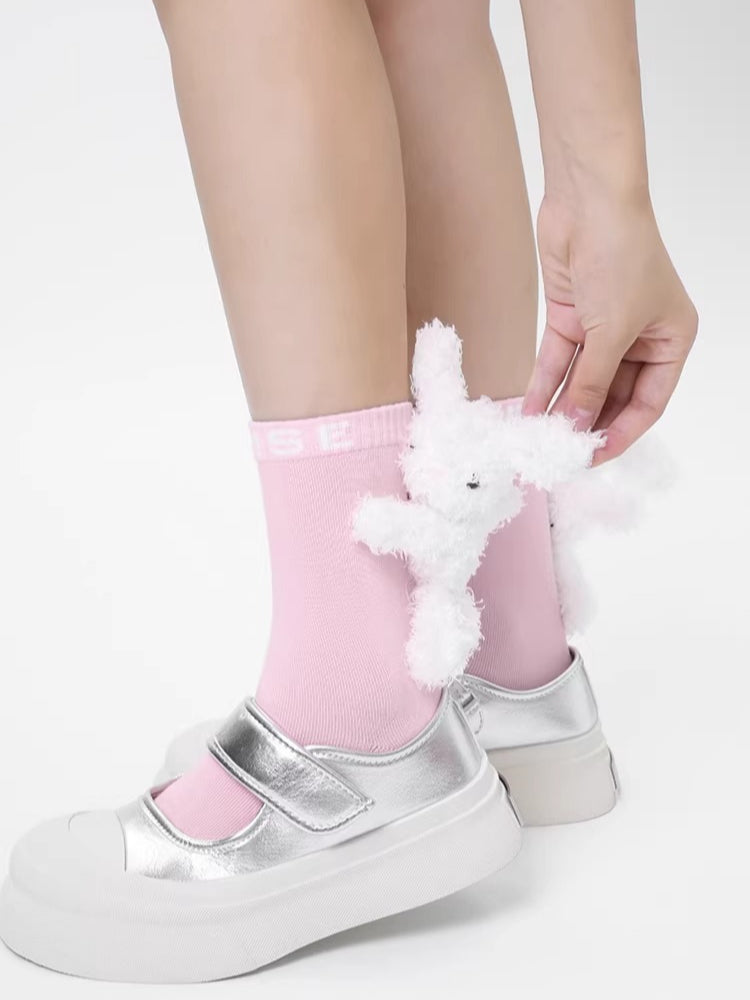 Close-up of a hand adjusting a white 3D plush bunny embellishment on a pink ankle sock
