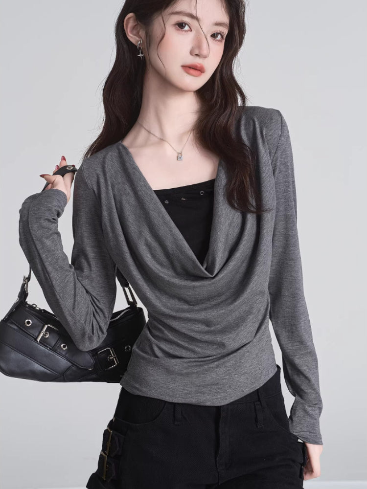 Model holding a black handbag while wearing a grey long-sleeved top with a draped neckline.