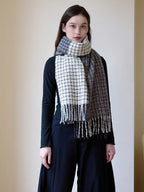 Woman wearing a black long-sleeve top and a plaid scarf with fringe detail, styled loosely around her neck.
