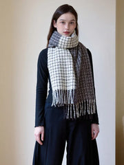 Woman wearing a black long-sleeve top and a plaid scarf with fringe detail, styled loosely around her neck.