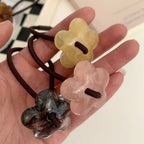 A hand holding three flower-shaped hair ties in yellow, pink, and grey marble patterns.