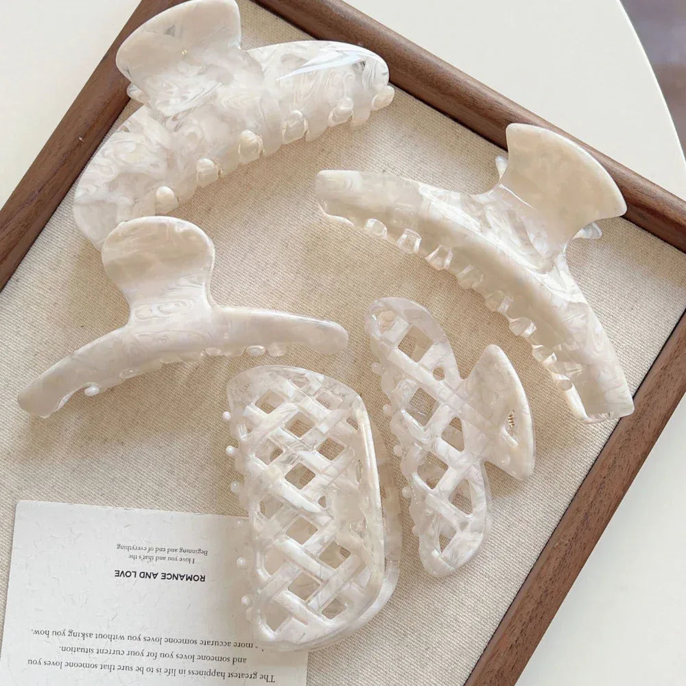 Several cream-colored marbled acetate hair clips and a pearl bracelet displayed on a wooden tray with a card.