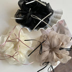 Three ruffled scrunchies in ivory, taupe, and black displayed on a white surface with decorative elements.