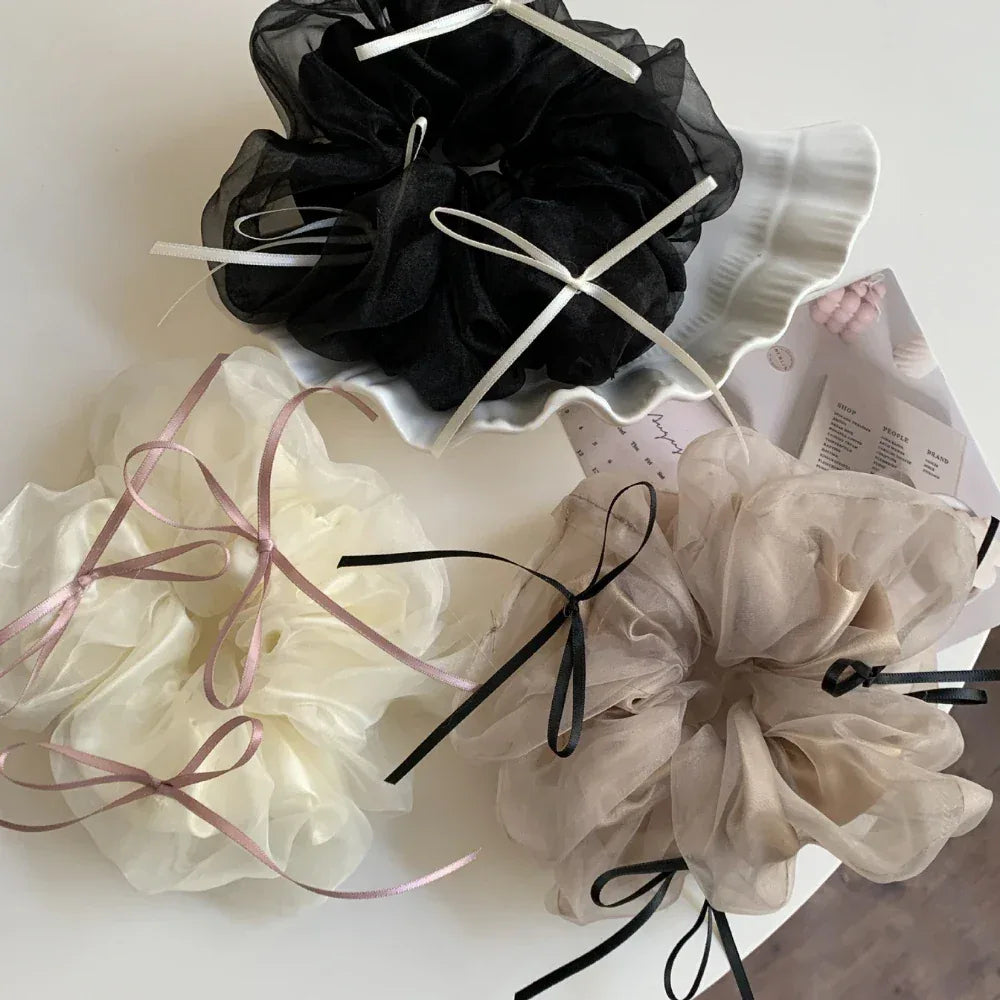Three ruffled scrunchies in ivory, taupe, and black displayed on a white surface with decorative elements.