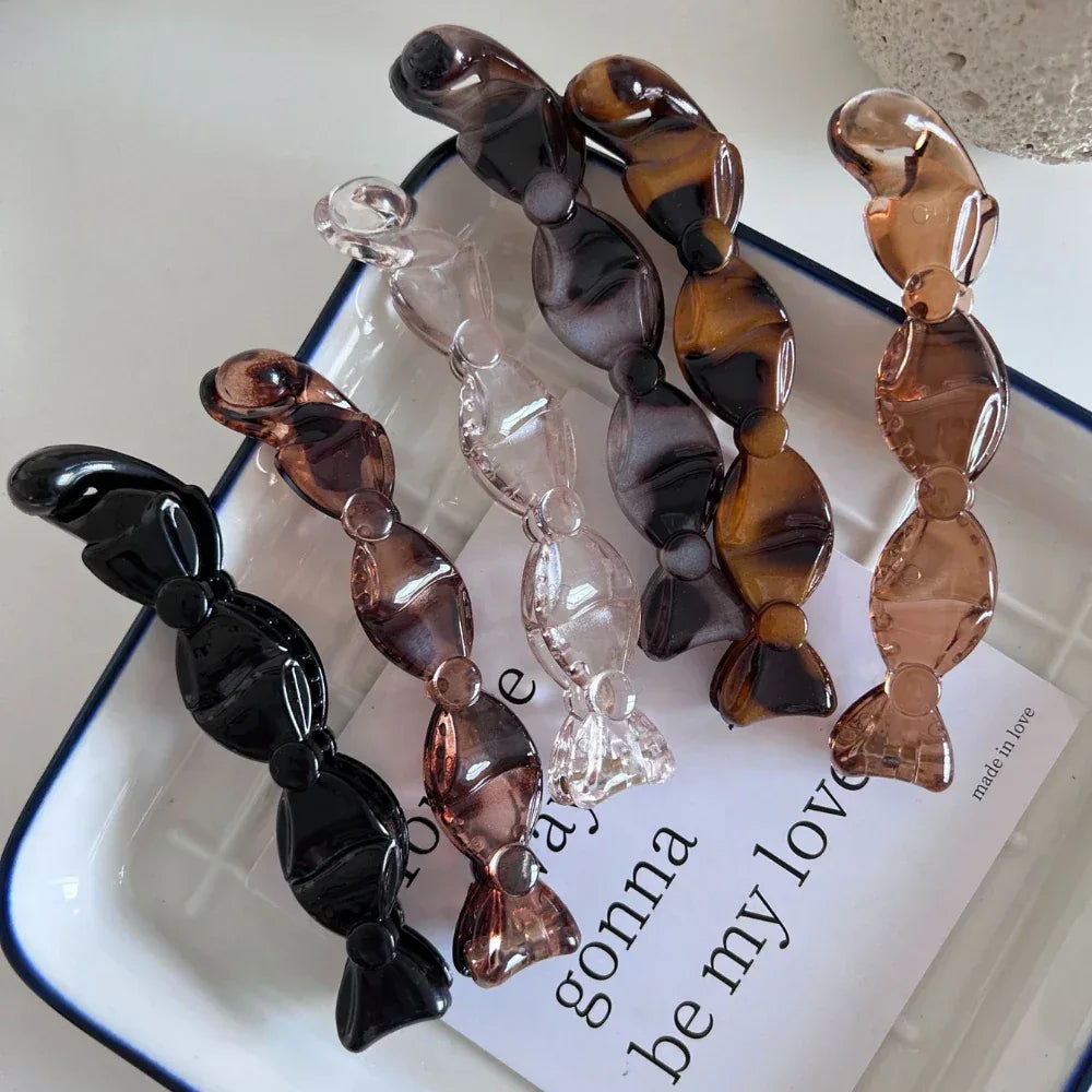 a group of candy-shaped hair clips in various colors including black, clear, brown, and marbled patterns arranged in a line