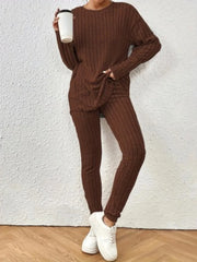 Woman in a brown ribbed knit loungewear set holding a white cup, standing against a white wall.