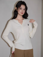 Woman wearing a white cable knit henley sweater with a black embroidered logo, paired with brown wide-leg pants.
