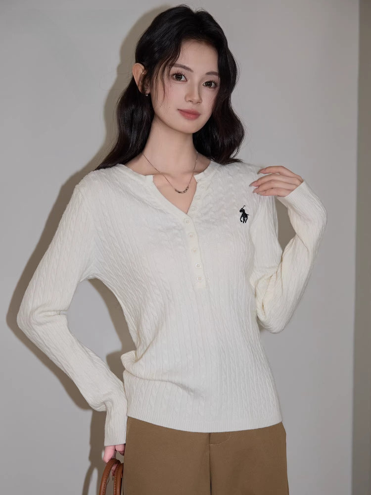 Woman wearing a white cable knit henley sweater with a black embroidered logo, paired with brown wide-leg pants.