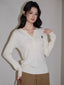 Woman wearing a white cable knit henley sweater with a black embroidered logo, paired with brown wide-leg pants.