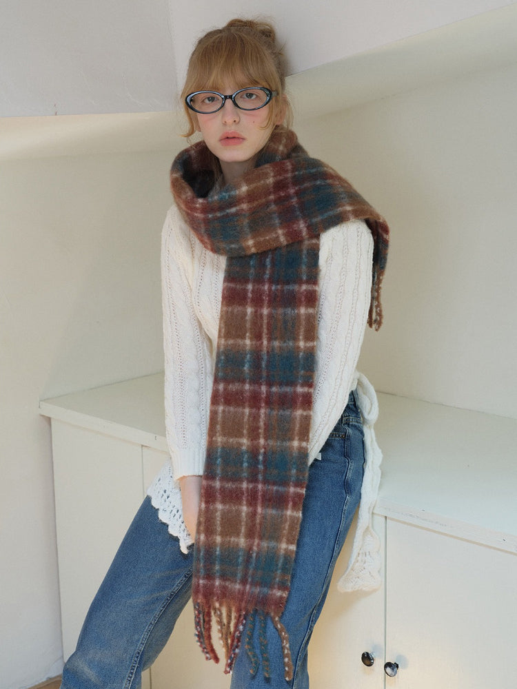 Model wearing a white cable knit cropped sweater, blue denim jeans, a plaid scarf, and glasses, leaning against a shelf. Main image
