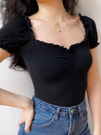 Woman wearing a black ribbed knit top with puffed short sleeves and a ruffled sweetheart neckline.