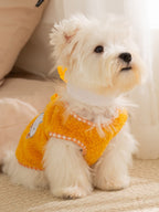 White dog wearing a yellow fleece vest with a checkered trim and embroidered applique.