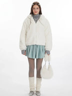Model wearing a white fuzzy hooded jacket with bunny ears, a grey turtleneck, a light blue pleated skirt, grey tights, and white leg warmers. She is holding a white fuzzy purse.