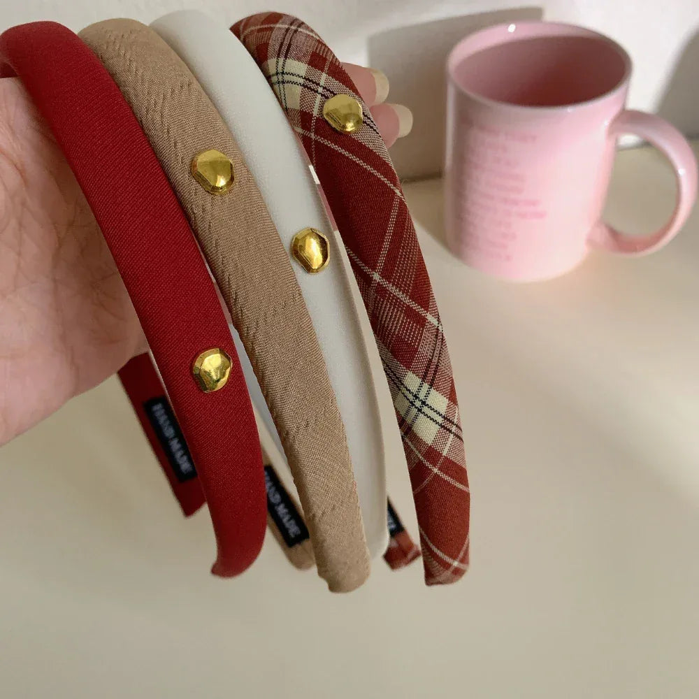 Hand holding a collection of padded headbands in red, beige, white, and plaid
