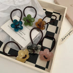A tray of flower-shaped hair ties in various translucent colors: blue, green, orange, grey, yellow, and pink.