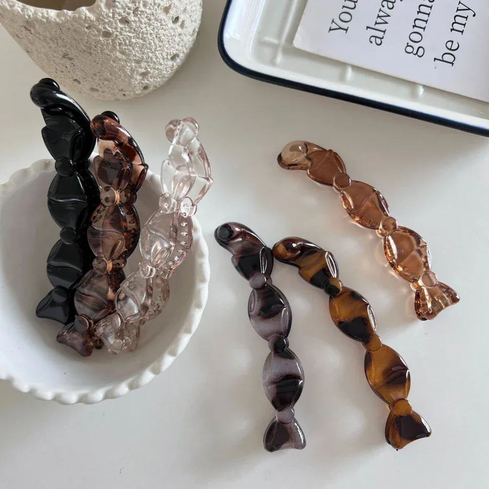 a close-up of several candy-shaped hair clips in different colors, some arranged in a white bowl and others on a white surface