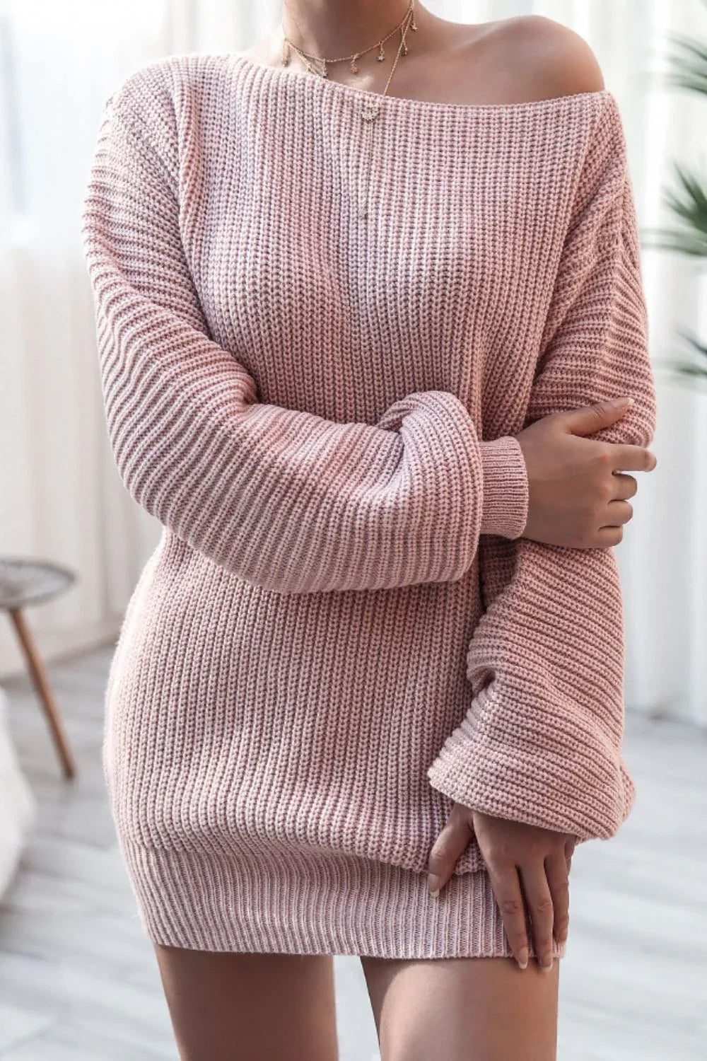 Woman with arms crossed wearing a pink off-the-shoulder ribbed knit tunic sweater.