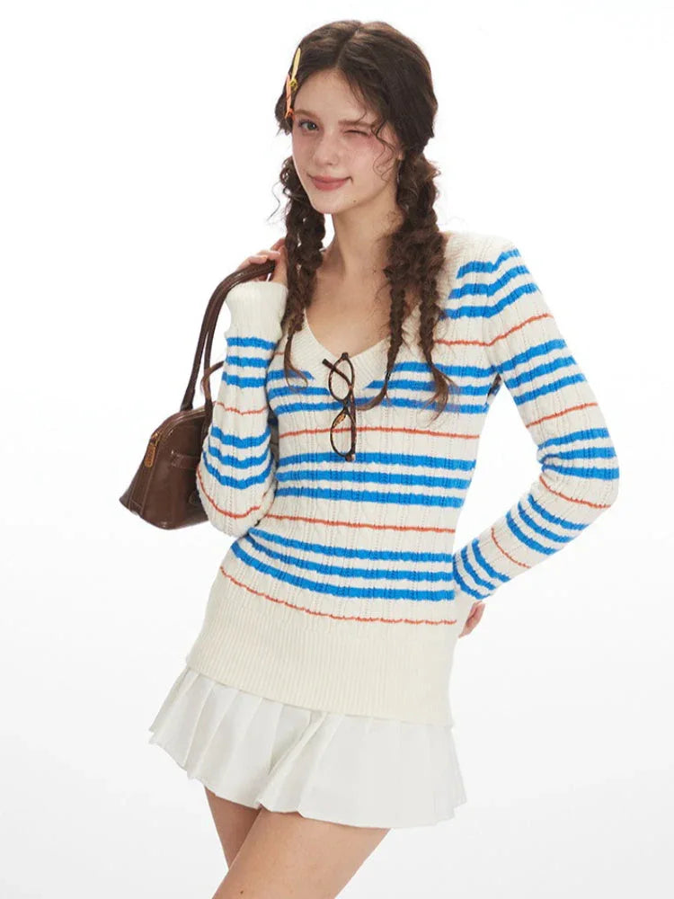 Woman wearing a striped v-neck sweater with a white ruffled skirt and beige leg warmers, holding a brown handbag and winking.