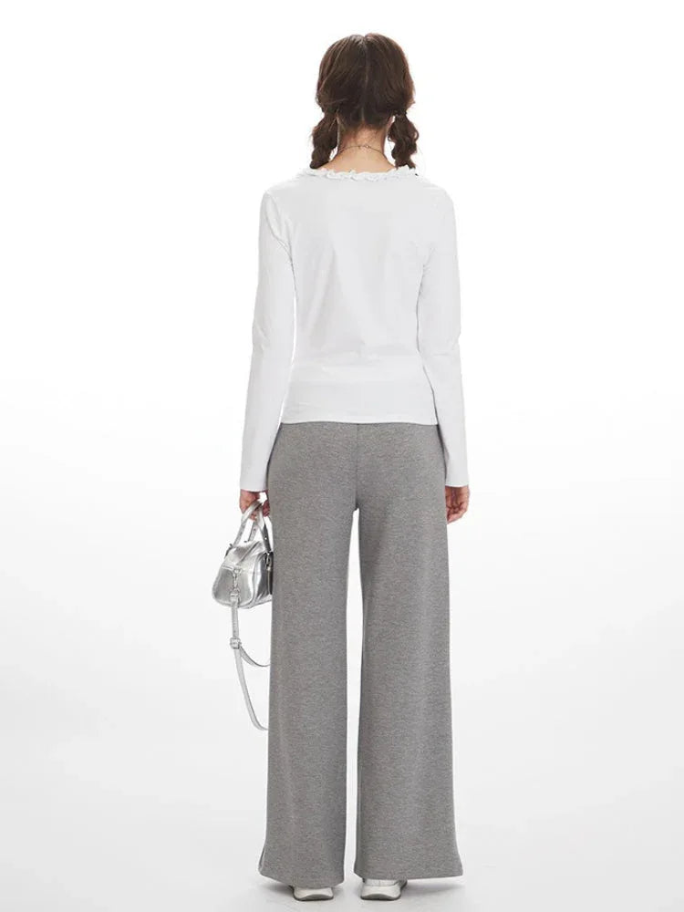 Back view of a woman wearing a white long-sleeve shirt and grey wide-leg sweatpants.