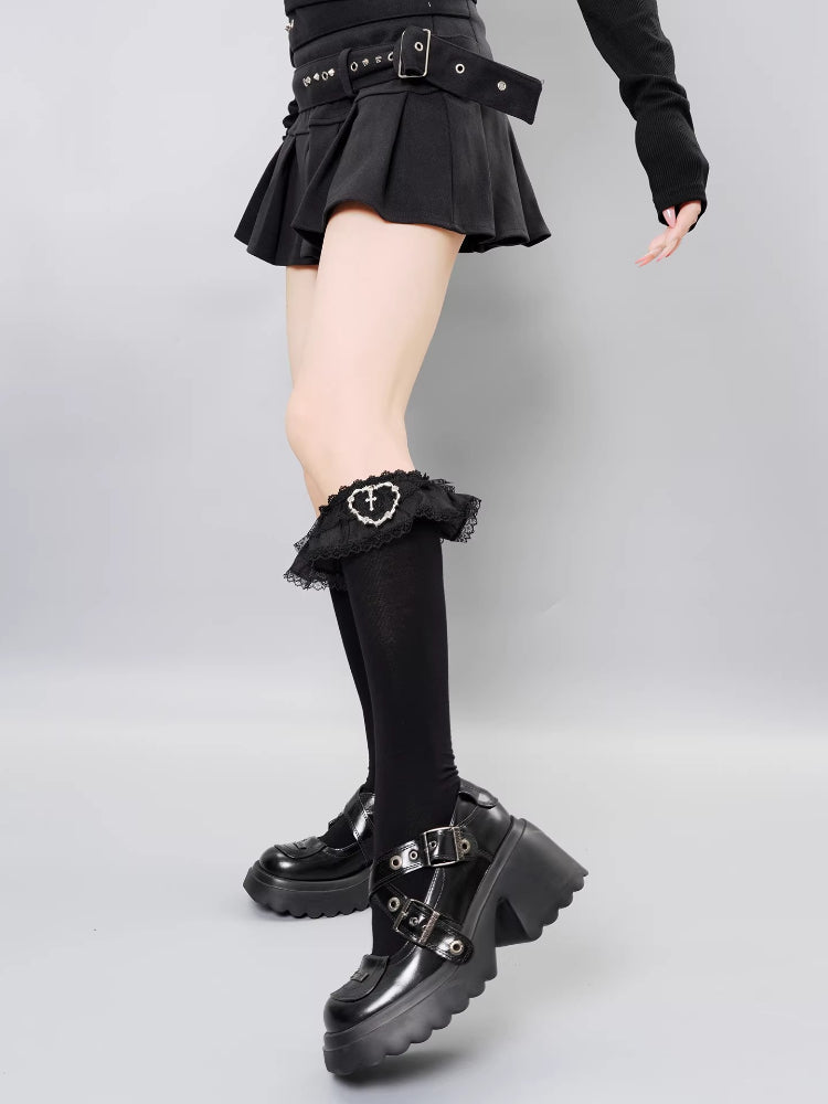 A model poses in a black pleated skirt, black knee-high socks, and statement platform shoes.