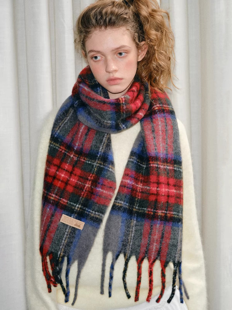 A young woman with curly hair tied in a ponytail, wearing a cream-colored sweater and a tartan plaid scarf.