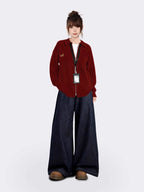 Full-body shot of a woman wearing a maroon zip-up knit cardigan, white t-shirt, and dark wash wide-leg jeans, standing against a white background.