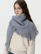 Model wearing a grey oversized scarf with fringe detail over a cream sweater
