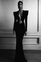 Woman wearing a long black dress with a deep V-neckline and a sparkling brooch at the waist.