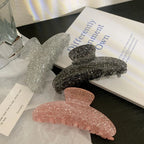 Three glitter claw clips in pink, black, and silver on a black surface with a book.