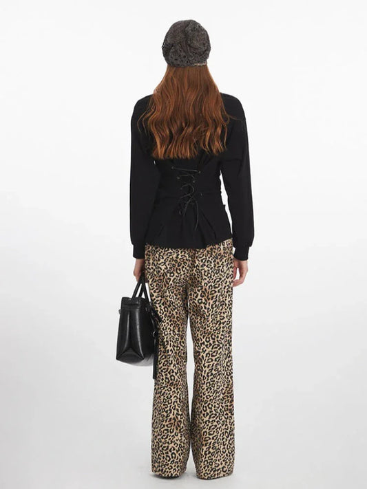 Woman wearing a black V-neck long-sleeved top with a lace-up back detail, leopard print wide-leg pants, a grey knit beanie, and carrying a black structured handbag, shown from the back.