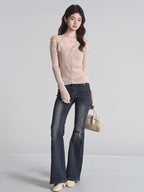 Full body shot of a woman wearing a beige ribbed knit cardigan with lace trim and a v-neck, paired with dark wash flared jeans and holding a beige handbag.
