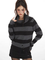Model wearing a grey and black striped sweater with a turtleneck, black shorts, black tights with stars, and black boots, touching her neck.