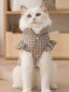 White cat wearing a brown plaid vest with ruffled sleeves and a high collar.