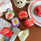 A flat lay of fruit-shaped hair clips scattered on a table with a newspaper and a mug.