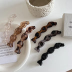 a top-down view of multiple candy-shaped hair clips in different colors and patterns on a white surface, with a decorative stone and a small box in the background