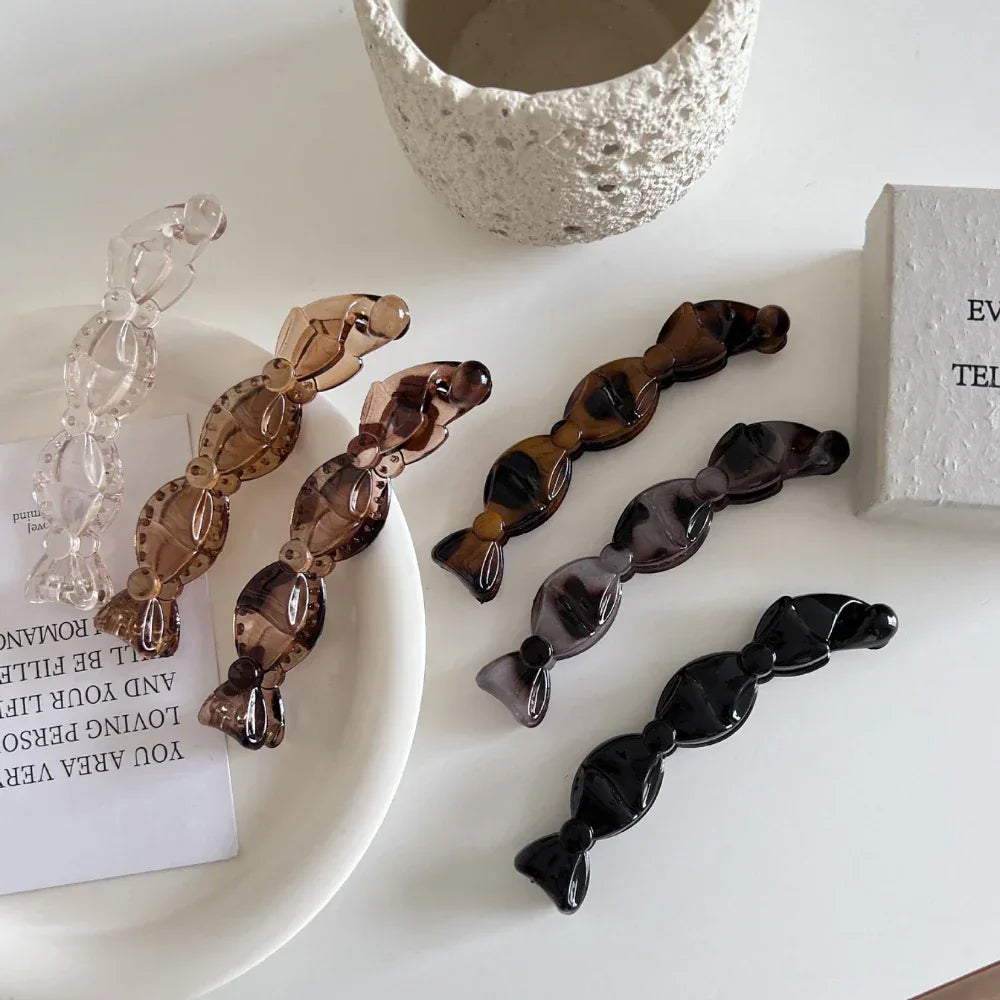 a top-down view of multiple candy-shaped hair clips in different colors and patterns on a white surface, with a decorative stone and a small box in the background