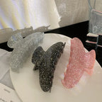 Three glitter claw clips in pink, black, and silver arranged on a white plate.