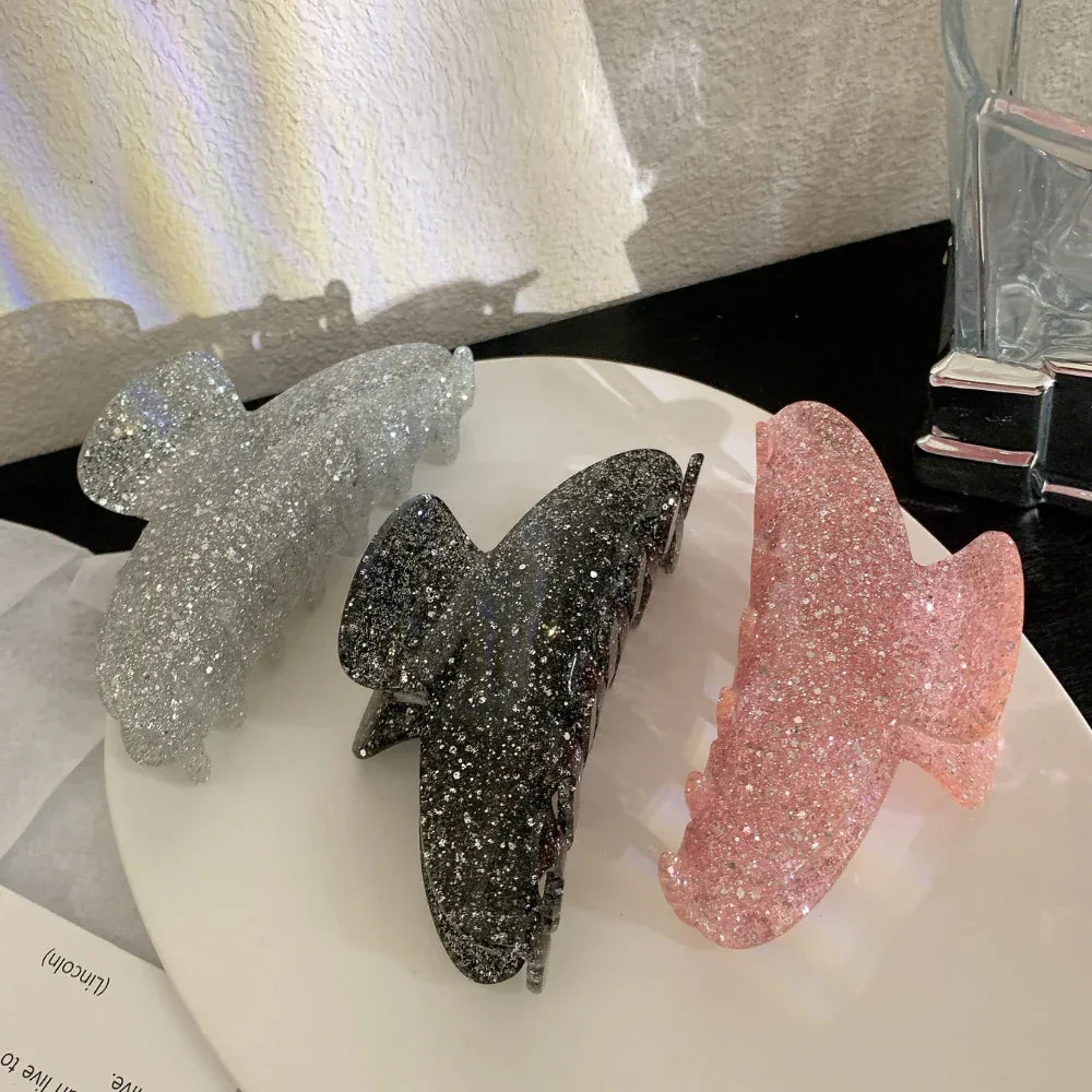 Three glitter claw clips in pink, black, and silver arranged on a white plate.