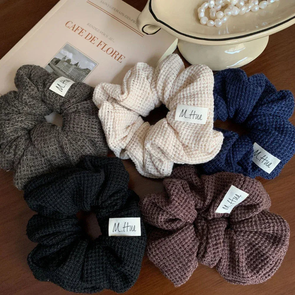 Collection of waffle knit scrunchies in various colors including black, beige, navy blue, dark brown, and grey