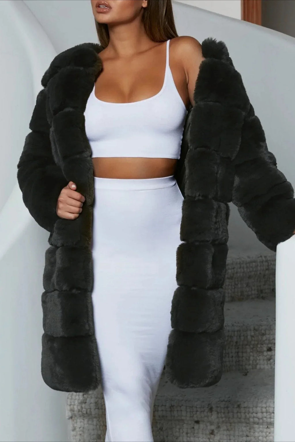 Woman wearing a gray faux fur coat over a white crop top and white pencil skirt.