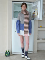 Model wearing a layered outfit with a grey cropped sweater over a blue checkered shirt, white ruffled skirt, striped scarf, and white Mary Jane shoes.