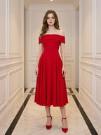 Woman wearing a red off-the-shoulder midi dress with flared skirt and red heels, standing in a hallway.